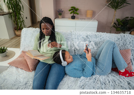 Mother and daughter relaxing on couch at home 134635718