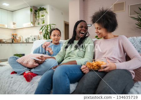 Black family enjoying snacks and laughing on sofa at home 134635719