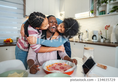 Mother and daughters enjoying hugging and laughing in kitchen 134635729