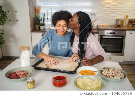 Mother kissing daughter while making homemade pizza Mother kissing daughter while making homemade pizza 134635759