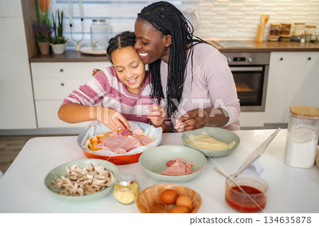Mother and daughter cooking pizza together in kitchen 134635878