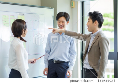 一群面帶笑容的日本商務團隊成員正在辦公室的白板前熱烈討論。 134635981