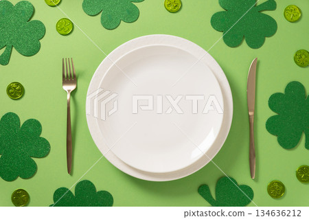 St Patrick's Day table setting with empty white plate and traditional shamrock, clover leaves and coins on light green background. View from above. St Patrick's Day table setting with empty white plate and traditional shamrock, clover leaves and coins on light green background. View from above. 134636212