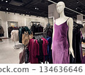 A modern fashion store interior features a mannequin dressed in a purple velvet dress surrounded by clothing racks 134636646