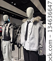 Two mannequins dressed in layered winter outfits stand inside a modern fashion store showcasing neutral seasonal styling 134636647