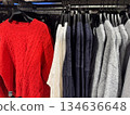 A rack of cozy knit sweaters in red white navy and gray tones is neatly arranged in a clothing store 134636648