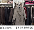 A classic plaid coat is displayed among neatly organized neutral toned garments in a fashion retail store 134636650