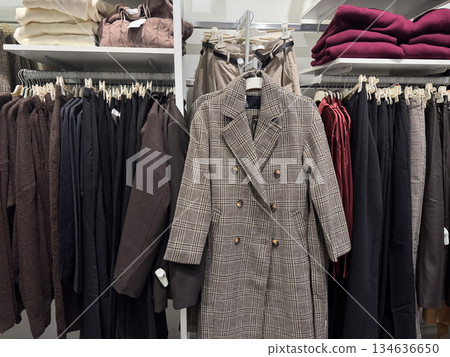 A classic plaid coat is displayed among neatly organized neutral toned garments in a fashion retail store A classic plaid coat is displayed among neatly organized neutral toned garments in a fashion retail store 134636650