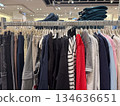 A full rack of mixed casual clothing in neutral and accent colors is displayed in a bright modern fashion store 134636651