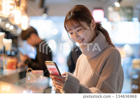 一位微笑的女士在咖啡館櫃檯使用智慧型手機進行無現金支付。 134636968