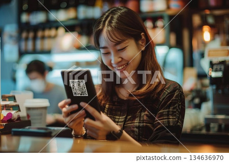 一位微笑的女士在咖啡館櫃檯使用智慧型手機進行無現金支付。 134636970