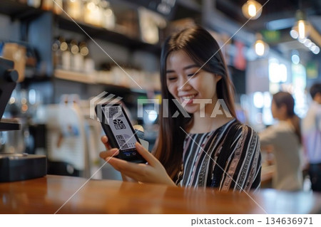 一位微笑的女士在咖啡館櫃檯使用智慧型手機進行無現金支付。 134636971