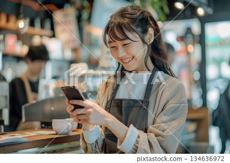 Smiling woman making a cashless payment using her smartphone at the counter of a cafe 134636972