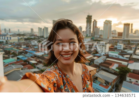 Young asian woman smiling while taking selfie, overlooking vibrant cityscape at sunset. Soft lighting highlights her cheerful expression. Neural network AI generated 134638571