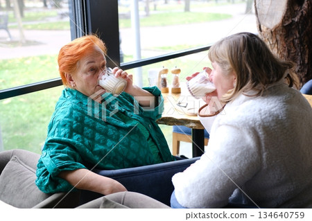 Two Diverse Young Women Enjoying a Meal and Drinks Together at a Cozy Cafe by the Window on a Bright Afternoon 134640759