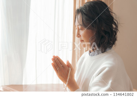 一位中年婦女在家中為逝者祈禱。 一位中年婦女在家中為逝者祈禱。 134641802