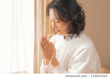 一位中年婦女在家中為逝者祈禱。 一位中年婦女在家中為逝者祈禱。 134641820