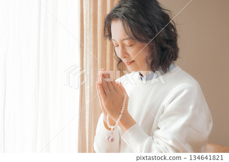 A middle-aged woman praying for the deceased at home A middle-aged woman praying for the deceased at home 134641821