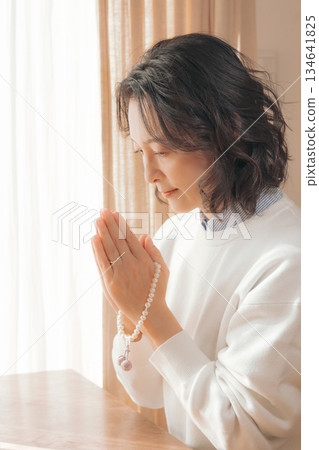 一位中年婦女在家中為逝者祈禱。 一位中年婦女在家中為逝者祈禱。 134641825