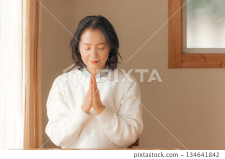 A middle-aged woman praying for the deceased at home A middle-aged woman praying for the deceased at home 134641842