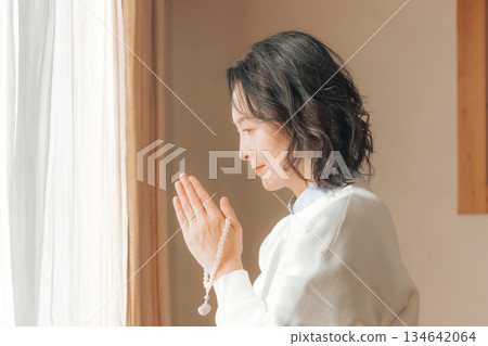 A middle-aged woman praying for the deceased at home A middle-aged woman praying for the deceased at home 134642064