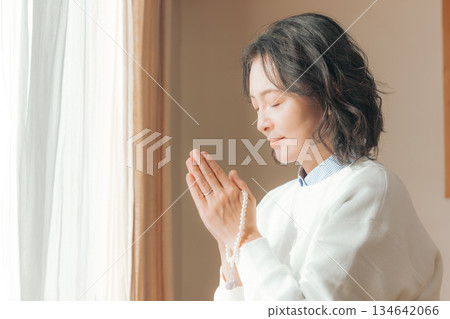 A middle-aged woman praying for the deceased at home A middle-aged woman praying for the deceased at home 134642066