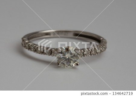 A white gold engagement ring featuring a round-cut diamond, with a pave diamond band for added brilliance. 134642719