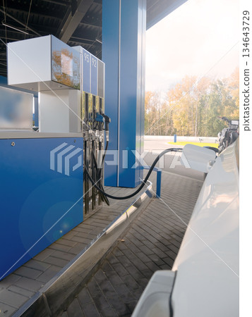 White car refuels at modern gas station with blue pump. Fueling vehicle energy demand and transportation concept. White car refuels at modern gas station with blue pump. Fueling vehicle energy demand and transportation concept. 134643729