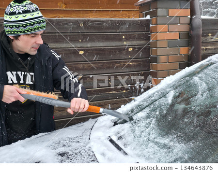 Man cleaning car from snow and ice with brush and scraper on winter morning. Daily routine during cold season. Man cleaning car from snow and ice with brush and scraper on winter morning. Daily routine during cold season. 134643876