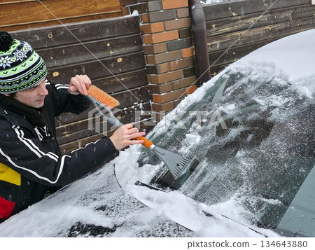Guy clearing snow and ice from car window with special brush and scraper in winter. Everyday routine during cold season. Guy clearing snow and ice from car window with special brush and scraper in winter. Everyday routine during cold season. 134643880