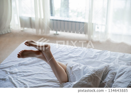 Female feet in bed. Young woman with beautiful legs in bedroom Female feet in bed. Young woman with beautiful legs in bedroom 134643885