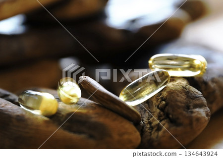 Yellow omega 3 softgel capsules on natural wood pieces. Health supplement for cardiac support and general wellness. Healthy life concept. Yellow omega 3 softgel capsules on natural wood pieces. Health supplement for cardiac support and general wellness. Healthy life concept. 134643924