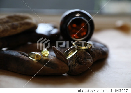 Golden omega capsules spilled from a dark bottle onto natural wood. Dietary supplement for health and wellness. Healthy lifestyle concept. Golden omega capsules spilled from a dark bottle onto natural wood. Dietary supplement for health and wellness. Healthy lifestyle concept. 134643927