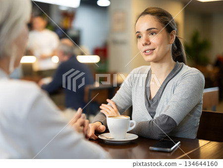 Girl in cafe sits near senior female companion, has nice conversation 134644160
