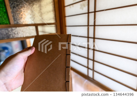 在日式房間裡拿著一本日文裝幀的筆記本 在日式房間裡拿著一本日文裝幀的筆記本 134644396