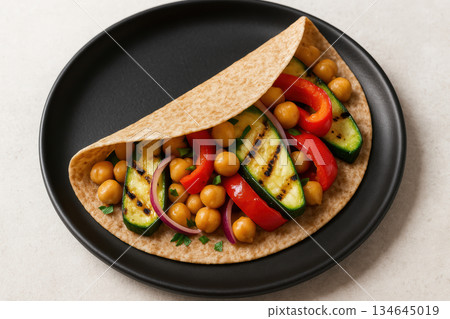 Whole wheat wrap filled with grilled zucchini, chickpeas, red bell pepper, and fresh onions on a black plate, AI Generative 134645019