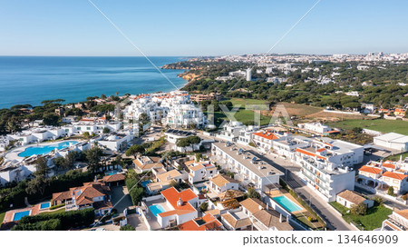 Aerial view of Olhos de Agua with whitewashed houses, resort pools and coastline leading to Falesia cliffs under clear blue sky in Albufeira, Algarve, Portugal. Concept of sunny beachside tourism 134646909
