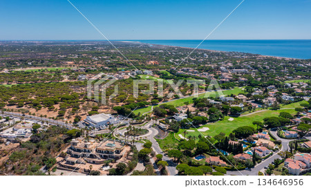 Aerial panorama of Vale do Lobo golf resort with luxurious villas, green fairways and pine forest stretching to the Atlantic coast under bright blue sky. Concept of elite tourism and real estate 134646956