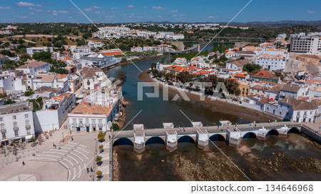 Aerial view of Tavira with historic Roman bridge over the Gilao River, traditional buildings and green hills in background under blue sky in Algarve, Portugal. Concept of cultural heritage tourism Aerial view of Tavira with historic Roman bridge over the Gilao River, traditional buildings and green hills in background under blue sky in Algarve, Portugal. Concept of cultural heritage tourism 134646968