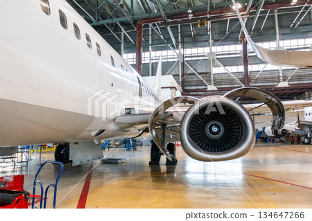 White passenger plane in the aircraft hangar. Airplane under maintenance. Checking mechanical systems for flight operations White passenger plane in the aircraft hangar. Airplane under maintenance. Checking mechanical systems for flight operations 134647266
