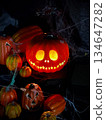 Spooky Illuminated Jack-o'-Lantern with Miniature Pumpkins and Spiderwebs on Black Background 134647282
