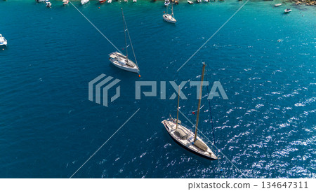 Aerial view of sailboats and yachts anchored in clear blue sea. Calm summer seascape with boats on turquoise water. Travel, vacation and marine lifestyle concept. Aerial view of sailboats and yachts anchored in clear blue sea. Calm summer seascape with boats on turquoise water. Travel, vacation and marine lifestyle concept. 134647311