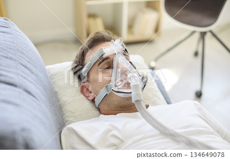 Man resting in bed with oxygen mask, receiving breathing support therapy at home Man resting in bed with oxygen mask, receiving breathing support therapy at home 134649078