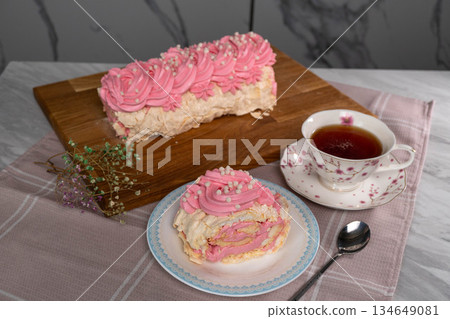 Pink meringue roll with rose swirl and cup of tea on checkered cloth Pink meringue roll with rose swirl and cup of tea on checkered cloth 134649081
