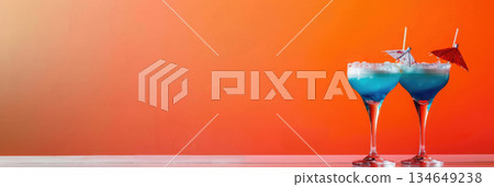 Two colorful cocktails with blue and red hues sit on a white surface against a vibrant orange background. copy space, free space for text 134649238