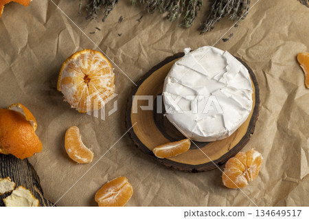 fresh white soft cheese with white mold lies on a wooden board on yellow paper, soft round cheese and juicy sweet orange tangerines fresh white soft cheese with white mold lies on a wooden board on yellow paper, soft round cheese and juicy sweet orange tangerines 134649517