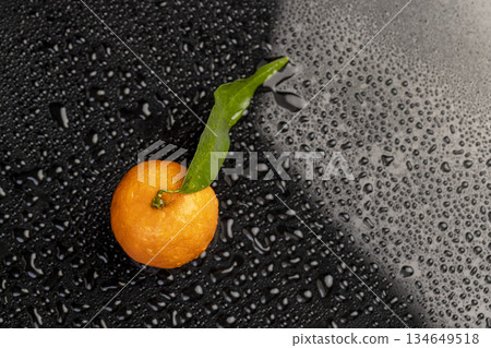 one ripe sweet tangerines with green leaves covered with drops of clear water with reflection on a black glass one ripe sweet tangerines with green leaves covered with drops of clear water with reflection on a black glass 134649518