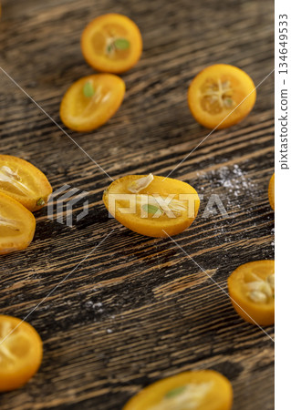 lots of ripe orange kumquat cut in half on a table, a group of scattered and sliced kumquat fruits on a wooden table and board lots of ripe orange kumquat cut in half on a table, a group of scattered and sliced kumquat fruits on a wooden table and board 134649533