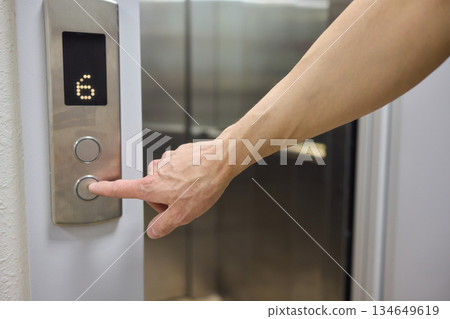 A Close Up Image of a Hand Passionately Pressing the Elevator Button in a Modern Building 134649619