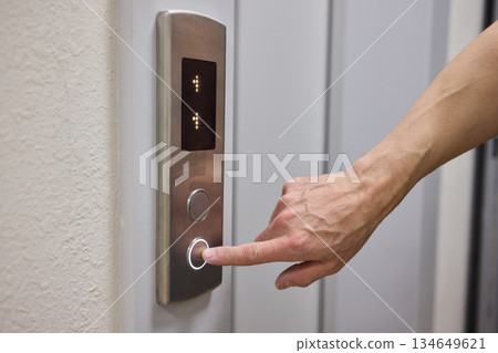 A Close Up Image of a Hand Passionately Pressing the Elevator Button in a Modern Building 134649621